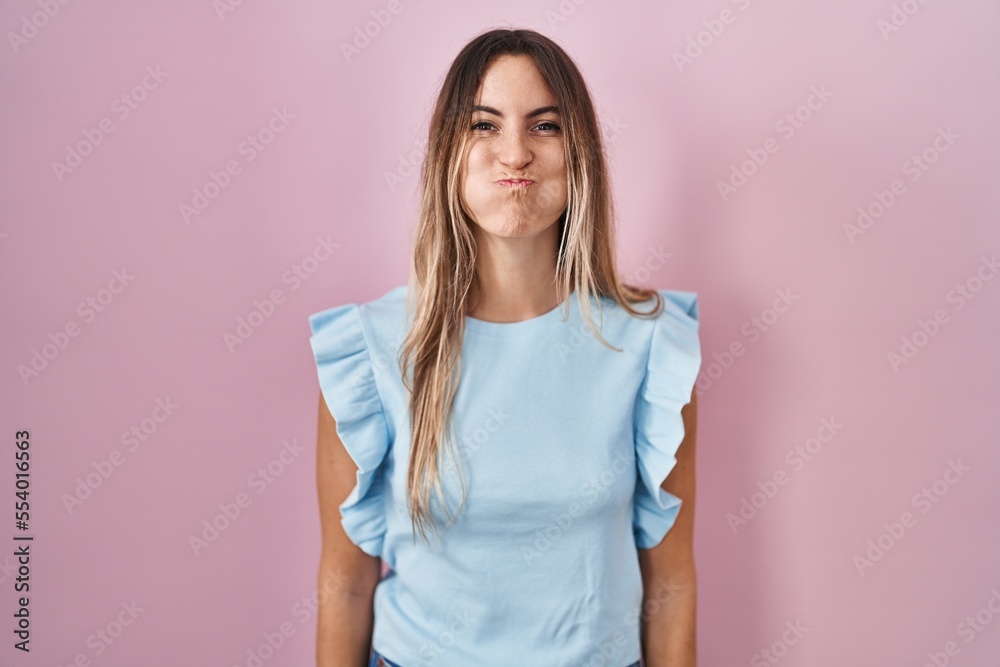 Young hispanic woman standing over pink background puffing cheeks with funny face. mouth inflated with air, crazy expression. Young hispanic woman standing over pink background puffing cheeks with funny face. mouth inflated with air, crazy expression.