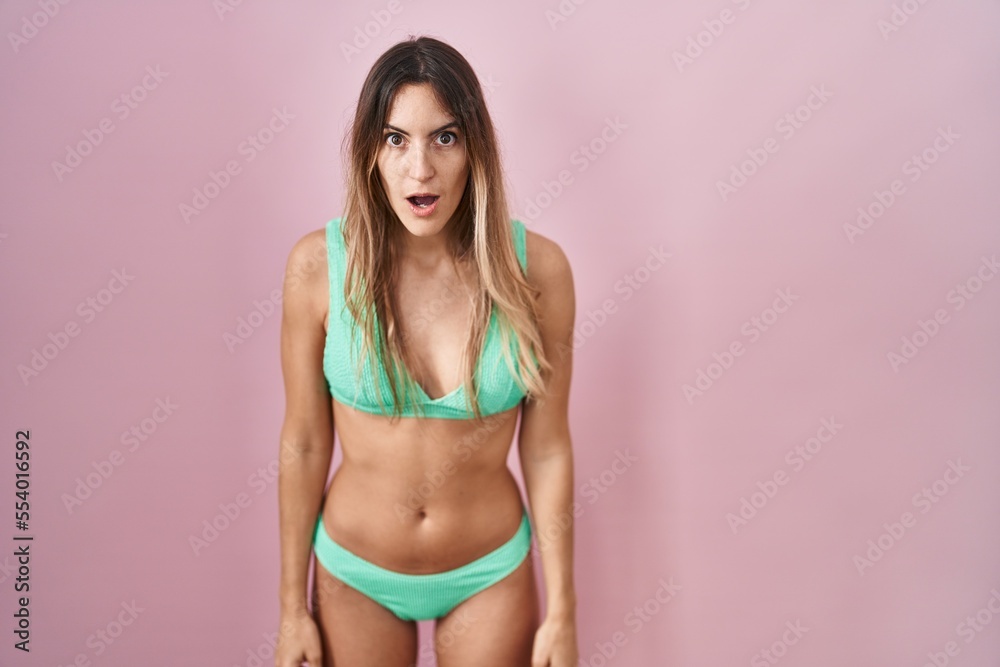 Fototapeta premium Young hispanic woman wearing bikini over pink background afraid and shocked with surprise and amazed expression, fear and excited face.