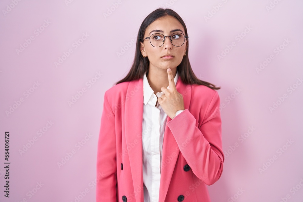 Young hispanic woman wearing business clothes and glasses thinking concentrated about doubt with finger on chin and looking up wondering Young hispanic woman wearing business clothes and glasses thinking concentrated about doubt with finger on chin and looking up wondering