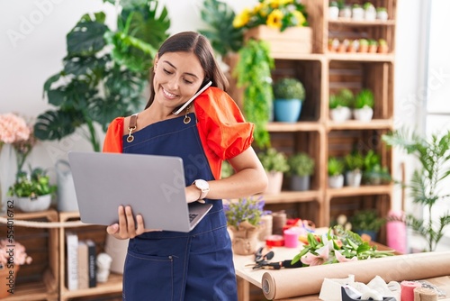 Young beautiful hispanic woman florist talking on smartphone using laptop at florist