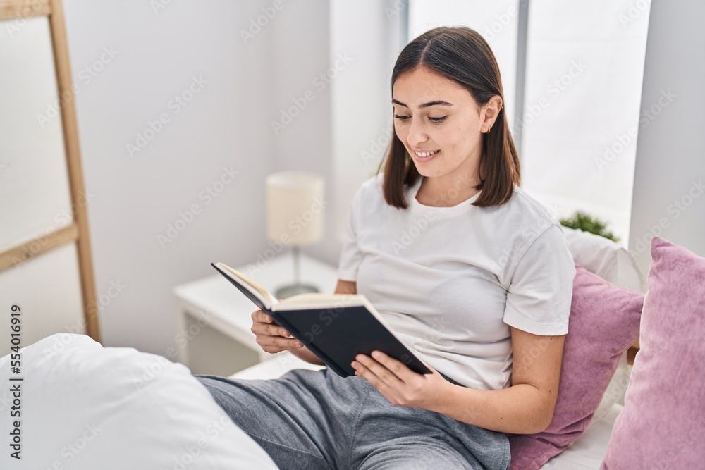 Young hispanic woman reading book sitting on bed at bedroom Young hispanic woman reading book sitting on bed at bedroom
