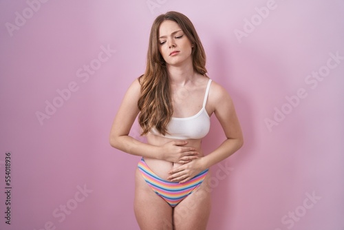 Caucasian woman wearing lingerie over pink background with hand on stomach because indigestion, painful illness feeling unwell. ache concept.