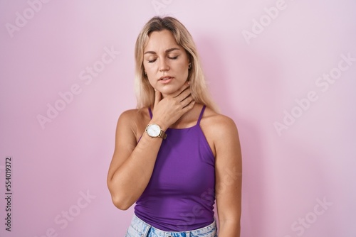Young blonde woman standing over pink background touching painful neck  sore throat for flu  clod and infection