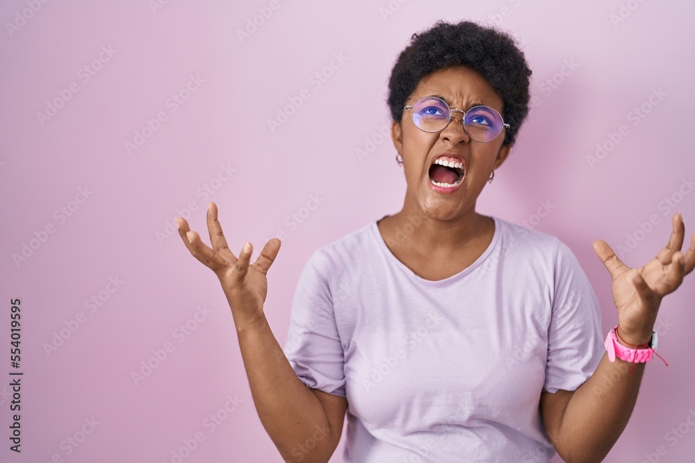 Young african american woman standing over pink background crazy and mad shouting and yelling with aggressive expression and arms raised. frustration concept. Young african american woman standing over pink background crazy and mad shouting and yelling with aggressive expression and arms raised. frustration concept.