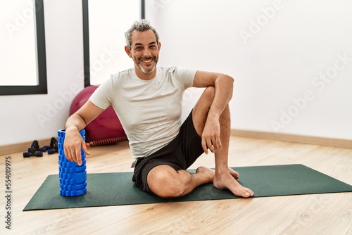 Middle age grey-haired man smiling confident leaning on foam roller at sport center