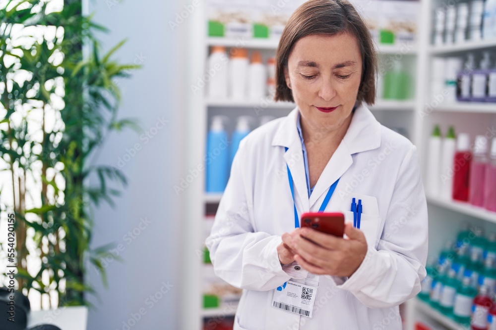 Middle age woman pharmacist using smartphone working at pharmacy Middle age woman pharmacist using smartphone working at pharmacy