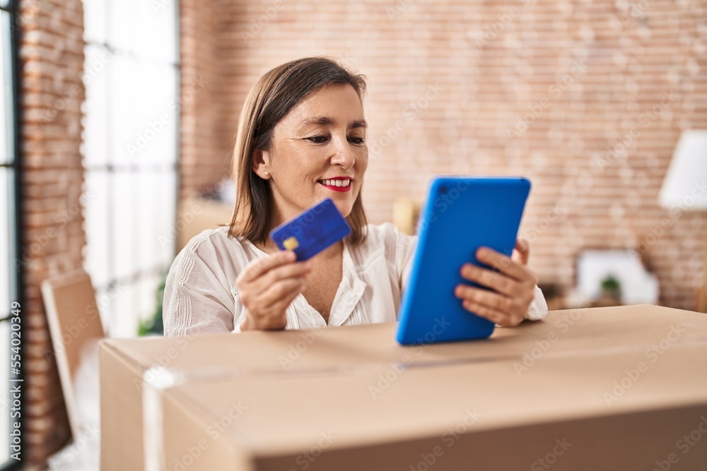 Middle age woman using touchpad and credit card standing at new home Middle age woman using touchpad and credit card standing at new home