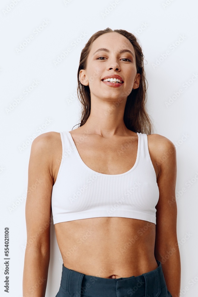 A woman poses on a white wall background in pants and T-shirt and smiles beautifully at home. Healthy and beautiful facial and body skin