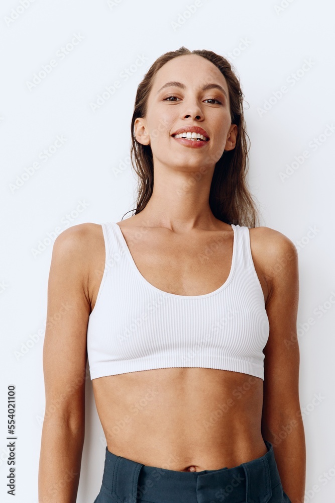A woman poses on a white wall background in pants and T-shirt and smiles beautifully at home. Healthy and beautiful facial and body skin A woman poses on a white wall background in pants and T-shirt and smiles beautifully at home. Healthy and beautiful facial and body skin