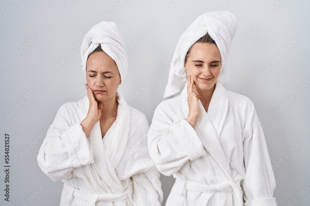 Middle age woman and daughter wearing white bathrobe and towel touching mouth with hand with painful expression because of toothache or dental illness on teeth. dentist Middle age woman and daughter wearing white bathrobe and towel touching mouth with hand with painful expression because of toothache or dental illness on teeth. dentist