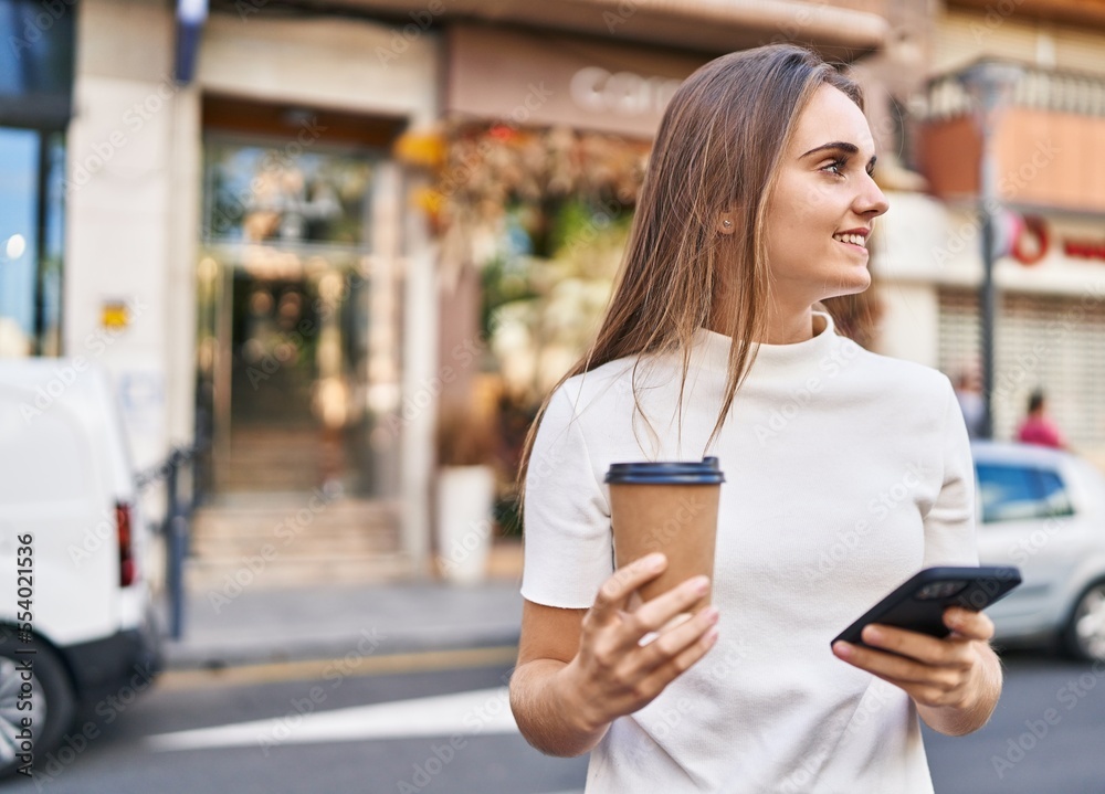 Young blonde woman using smartphone and drinking coffee at street