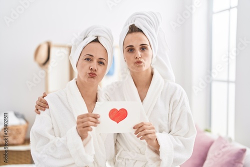 Middle age woman and daughter wearing bath robe holding heart card looking at the camera blowing a kiss being lovely and sexy. love expression.