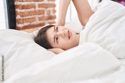 Young caucasian woman covering ears for noise at bedroom