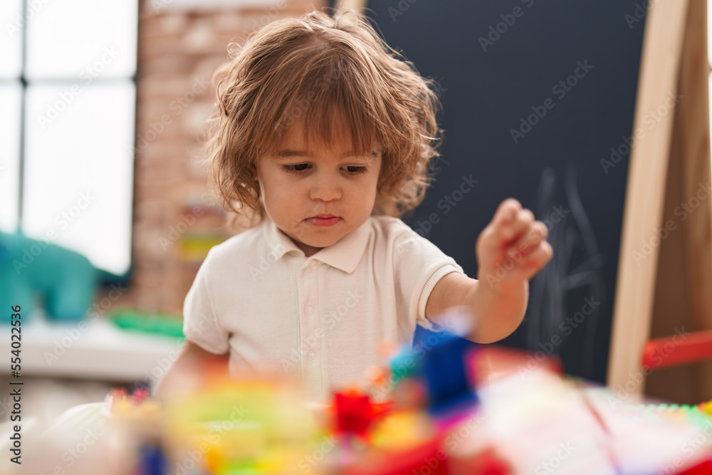 Adorable hispanic toddler playing with construction blocks standing at kindergarten