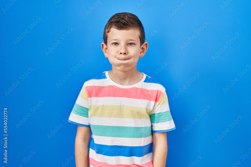 Young caucasian kid standing over blue background puffing cheeks with funny face. mouth inflated with air, crazy expression. Young caucasian kid standing over blue background puffing cheeks with funny face. mouth inflated with air, crazy expression.