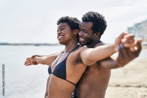 African american man and woman couple wearing swimsuit with arms open at seaside