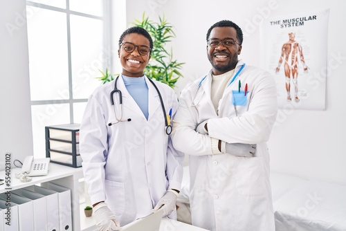 Young african american doctors working at medical clinic looking positive and happy standing and smiling with a confident smile showing teeth