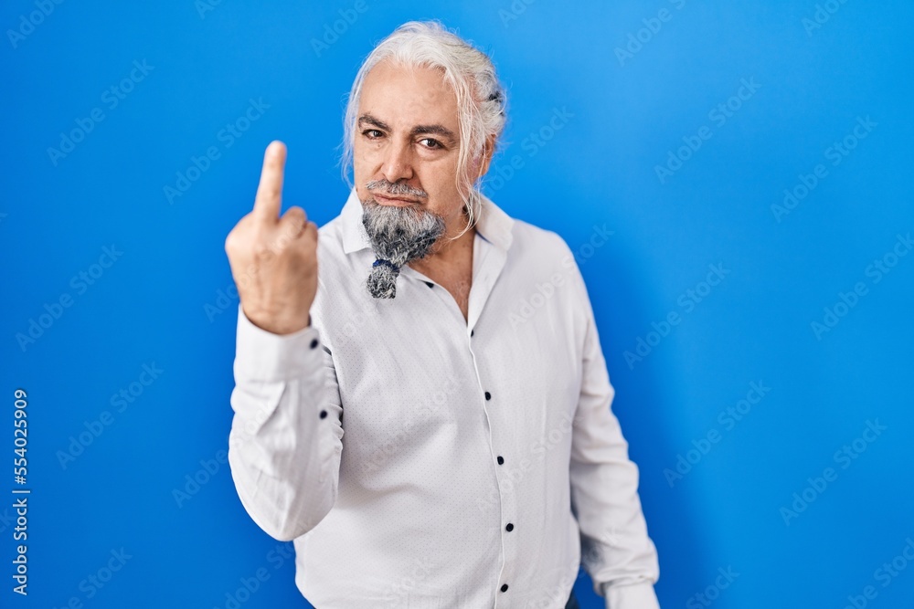 Middle age man with grey hair standing over blue background showing middle finger, impolite and rude fuck off expression