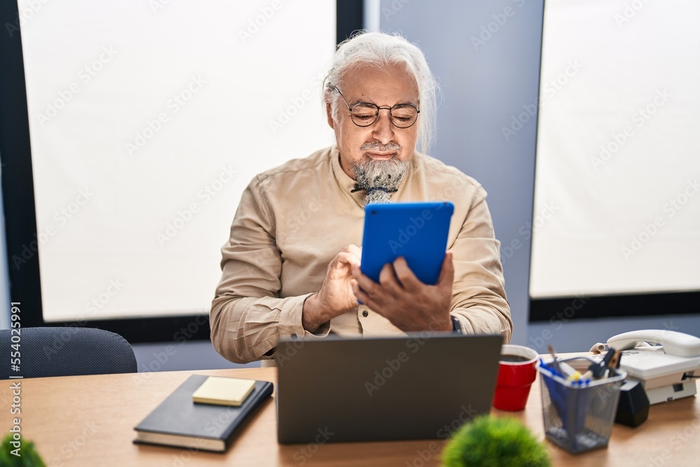 Middle age grey-haired man business worker using touchpad and laptop at office Middle age grey-haired man business worker using touchpad and laptop at office