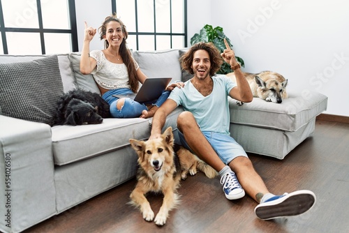 Wall Mural Young hispanic couple with dogs relaxing at home smiling amazed and surprised and pointing up with fingers and raised arms