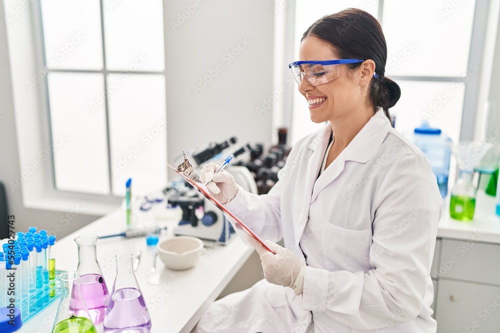 Young beautiful hispanic woman scientist smiling confident writing report working at laboratory