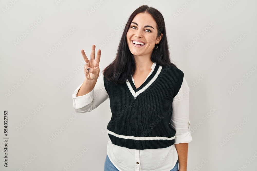 Young hispanic woman standing over isolated background showing and pointing up with fingers number three while smiling confident and happy.