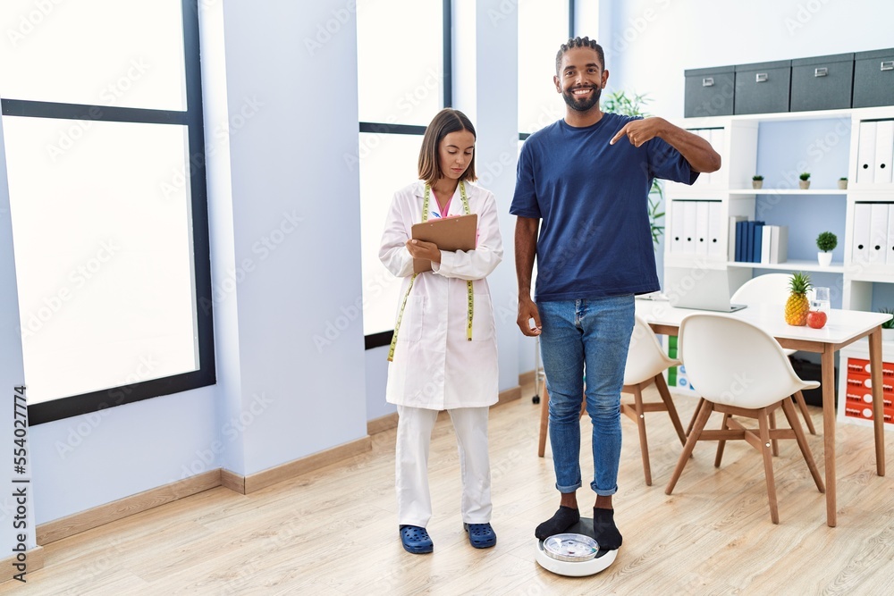 Dietitian at the clinic with client checking weight pointing finger to one self smiling happy and proud Dietitian at the clinic with client checking weight pointing finger to one self smiling happy and proud