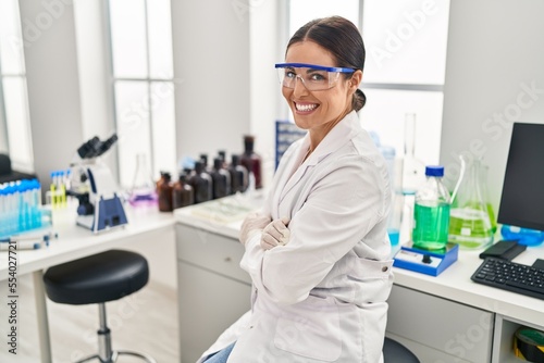 Young beautiful hispanic woman scientist smiling confident sitting with arms crossed gesture at laboratory
