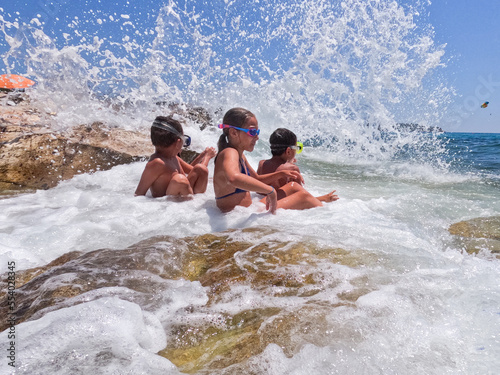 Children have fun on the beach with crashing and splashing sea waves. Summer childhood great time. 