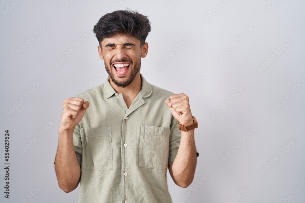 Arab man with beard standing over white background excited for success with arms raised and eyes closed celebrating victory smiling. winner concept. Arab man with beard standing over white background excited for success with arms raised and eyes closed celebrating victory smiling. winner concept.