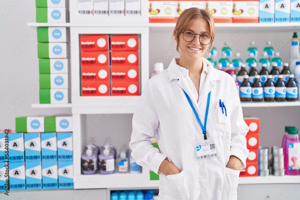 Young blonde girl pharmacist smiling confident standing at pharmacy