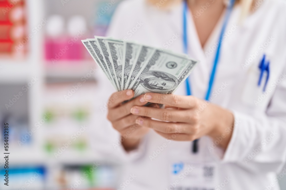 Young blonde woman pharmacist smiling confident holding dollars at pharmacy Young blonde woman pharmacist smiling confident holding dollars at pharmacy