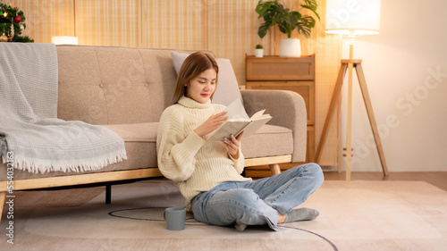Young asian woman drinking coffee and reading a book while wearing sweater and sitting to relaxation