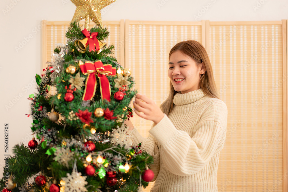 Young asian woman wearing sweater with smiling and decorating christmas tree in holiday with christmas
