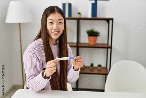 Young chinese girl holding pregnancy test sitting on the table at home.