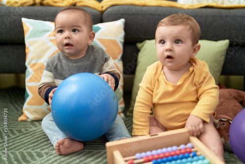 Two toddlers playing with balls and abacus sitting on floor at home