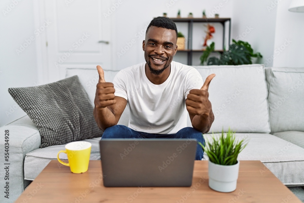 Young african man using laptop at home success sign doing positive gesture with hand, thumbs up smiling and happy. cheerful expression and winner gesture. Young african man using laptop at home success sign doing positive gesture with hand, thumbs up smiling and happy. cheerful expression and winner gesture.