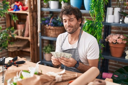 Young hispanic man florist smiling confident counting dollars at flower shop