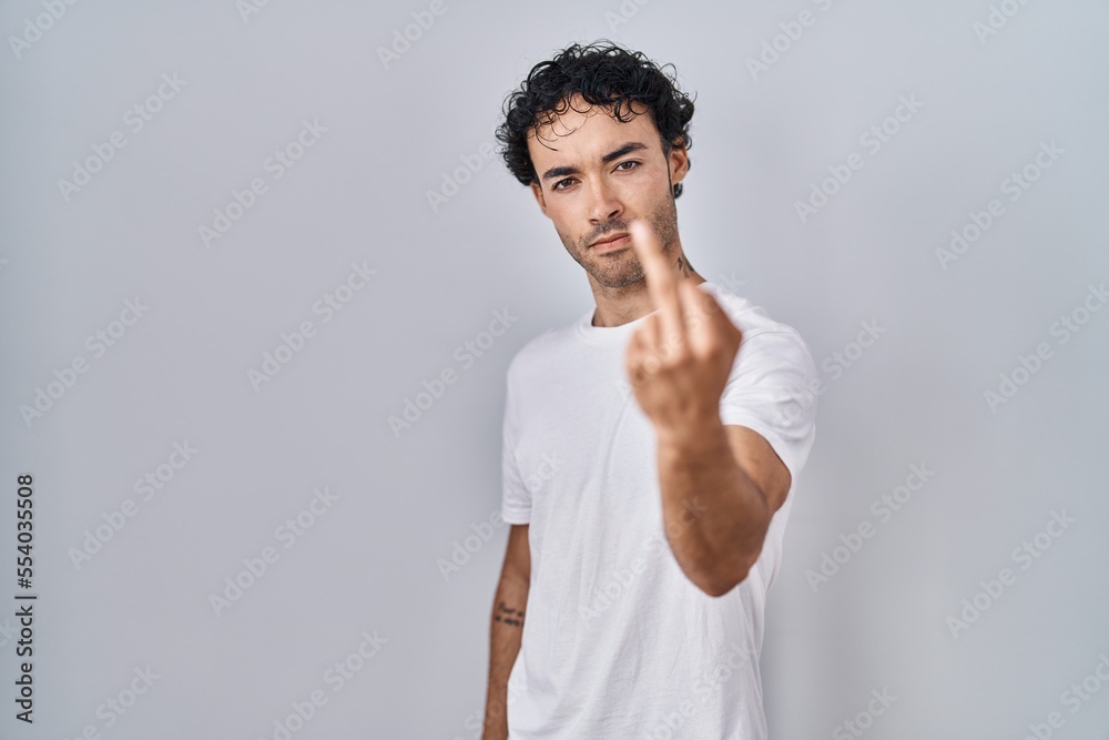 Hispanic man standing over isolated background showing middle finger, impolite and rude fuck off expression Hispanic man standing over isolated background showing middle finger, impolite and rude fuck off expression