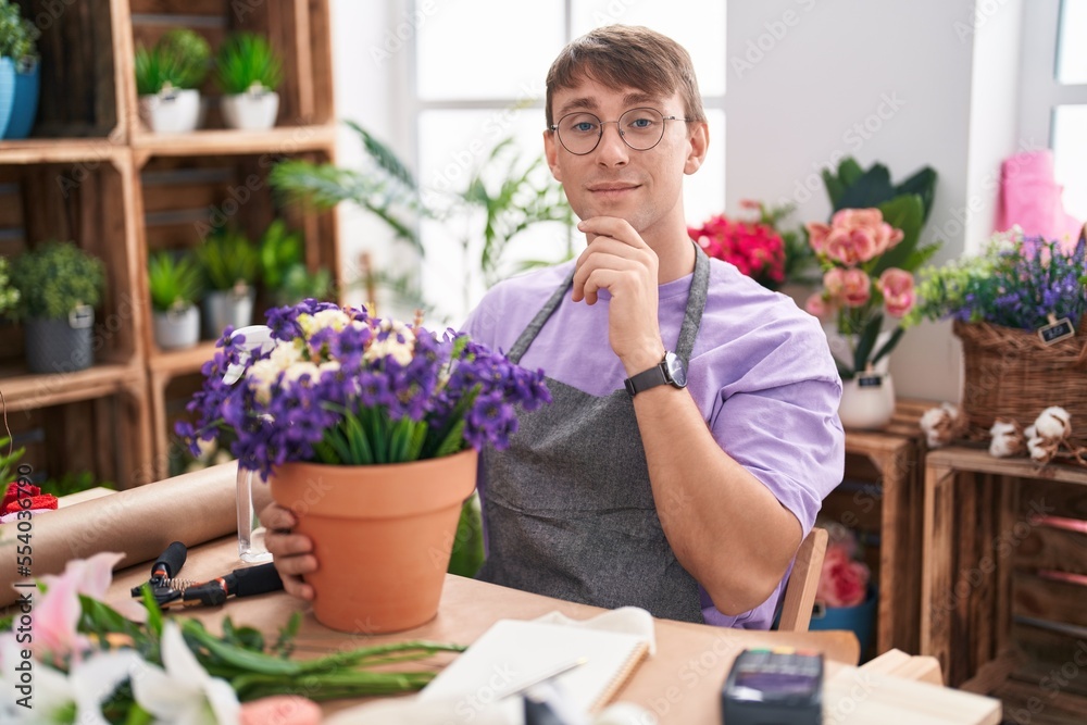 Caucasian blond man working at florist shop with hand on chin thinking about question, pensive expression. smiling and thoughtful face. doubt concept.