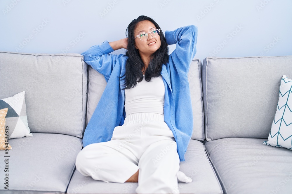 Obraz premium Young chinese woman relaxed with hands on head sitting on sofa at home