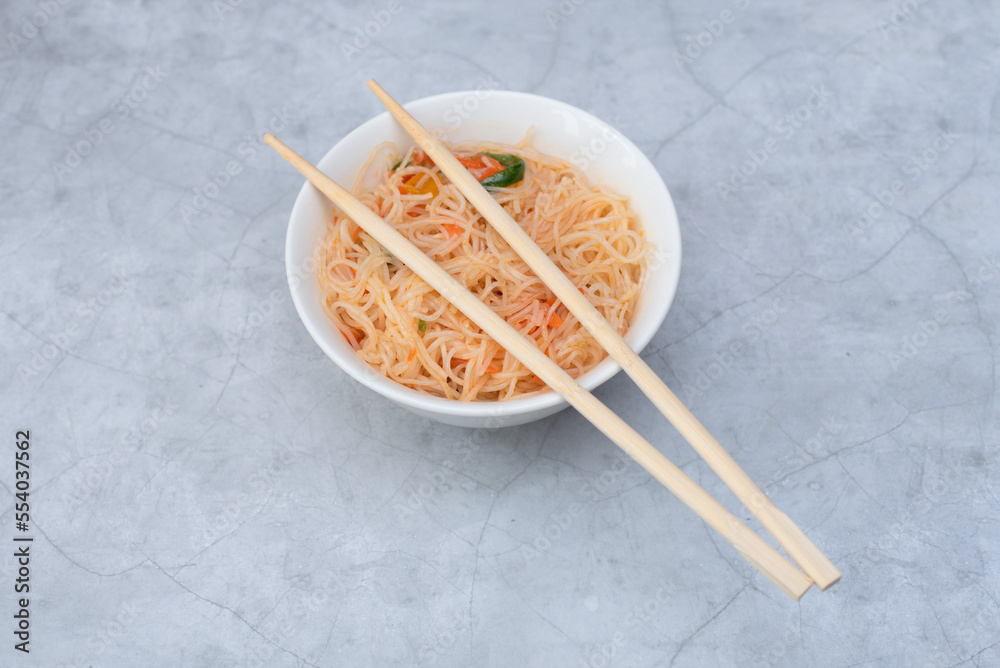 Delicious asian funchose salad in white bowl with wood sticks on grey background. Selective focus. Asian food concept Delicious asian funchose salad in white bowl with wood sticks on grey background. Selective focus. Asian food concept