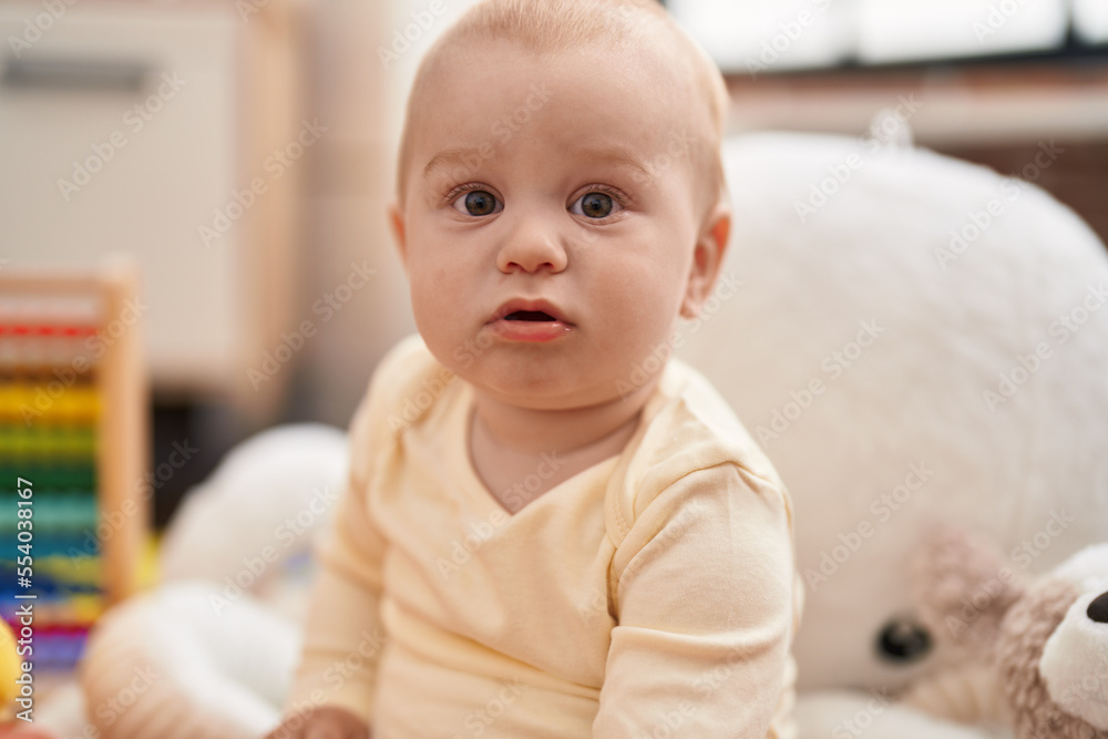 Adorable caucasian baby sitting on floor with relaxed expression at kindergarten Adorable caucasian baby sitting on floor with relaxed expression at kindergarten