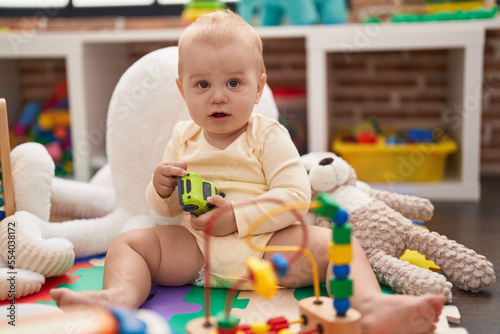 Adorable caucasian baby playing with car toy sitting on floor at kindergarten