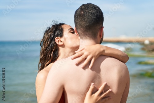 Young hispanic couple tourists wearing swimsuit hugging each other and kissing at seaside