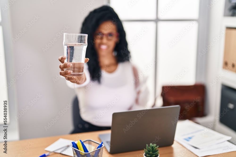 African american woman business worker using laptop holding glass of water at office African american woman business worker using laptop holding glass of water at office