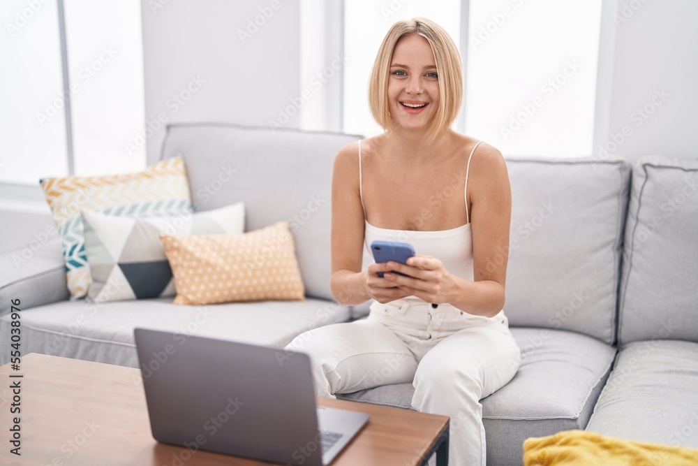 Young blonde woman using laptop and smartphone at home Young blonde woman using laptop and smartphone at home