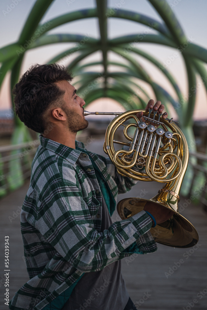 Musician walking on a bridge with his horn in his hand.