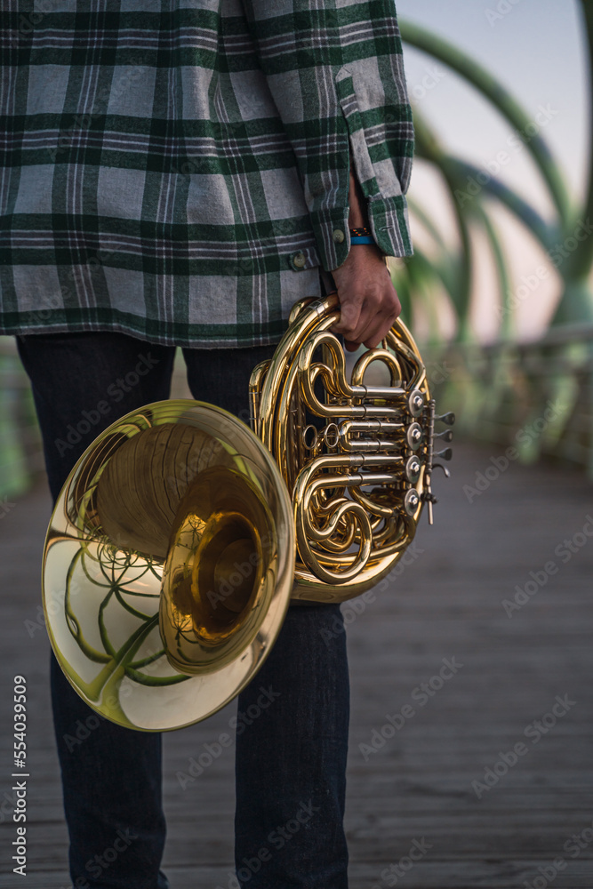 Musician walking on a bridge with his horn in his hand.