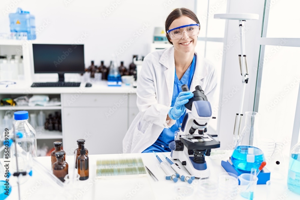 Young hispanic woman wearing scientist uniform using microscope at laboratory Young hispanic woman wearing scientist uniform using microscope at laboratory